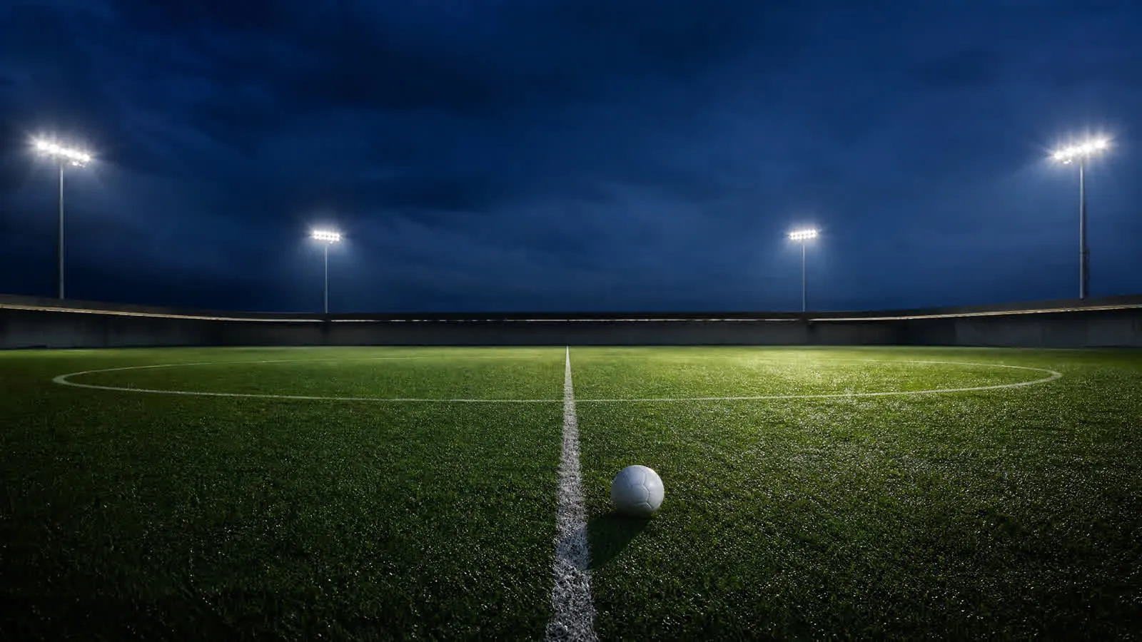 Nattlys over en ubrukt midtsirkel på en våt gressmatte, med en ball ved den hvite midtlinjen.